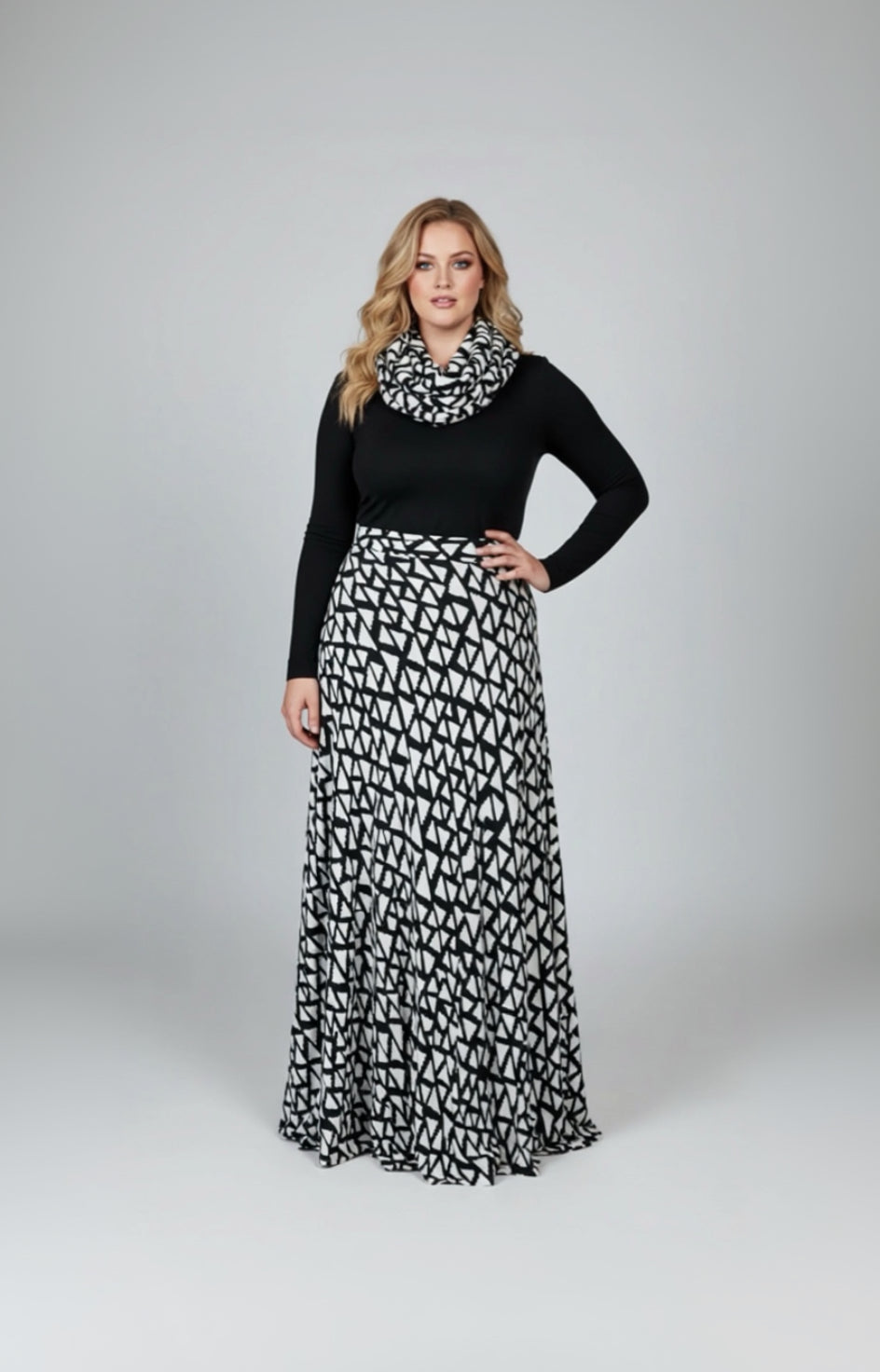 Woman wearing a black long-sleeve top and a long black and white patterned skirt on a white background