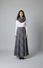 Woman wearing a long patterned skirt, white top, and gray scarf on a gray background