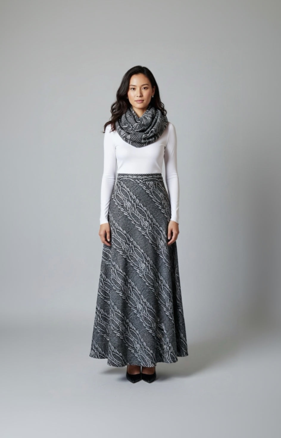Woman wearing a long patterned skirt, white top, and gray scarf on a gray background