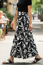 Woman walking on a city street wearing a black top and leaf-patterned skirt.