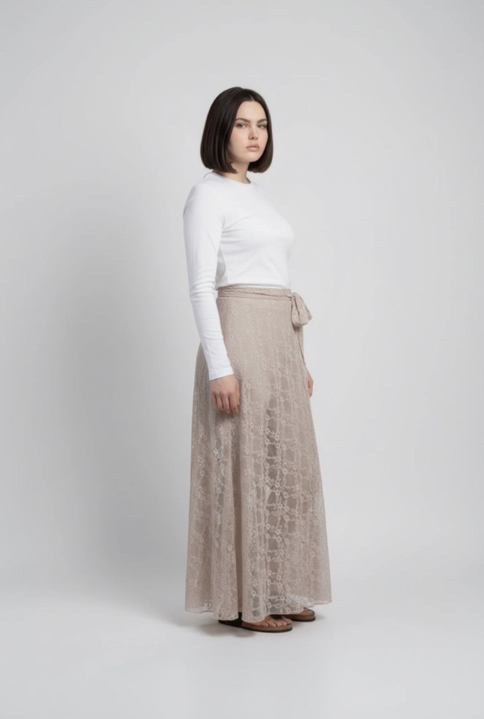 Woman wearing a white top and beige lace skirt on a plain background