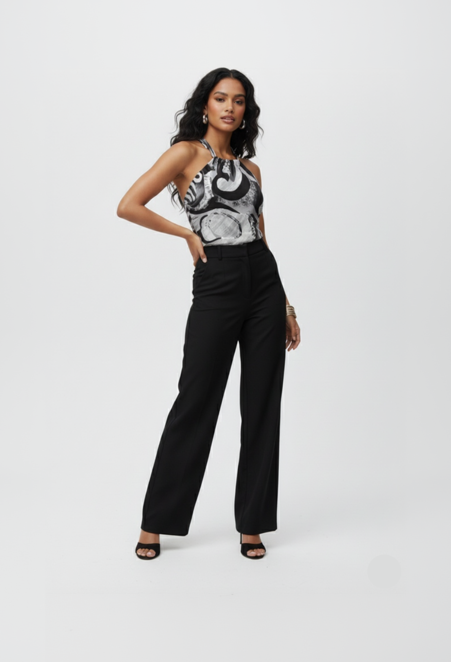 Woman wearing a black and white patterned top with high-waisted black pants on a white background