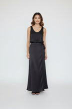 Woman wearing a black sleeveless top and long black satin skirt on a white background