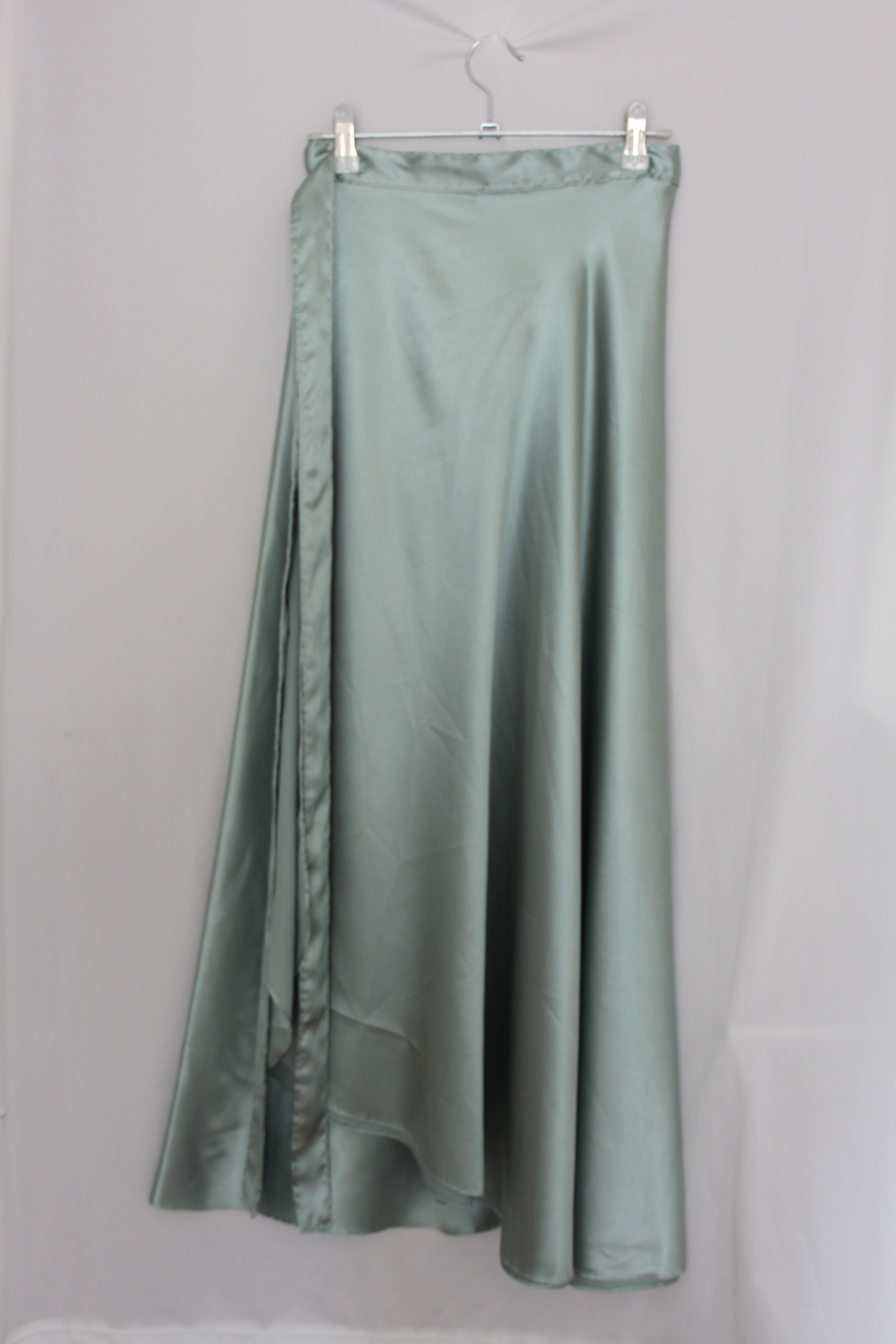 green satin skirt hanging on white background