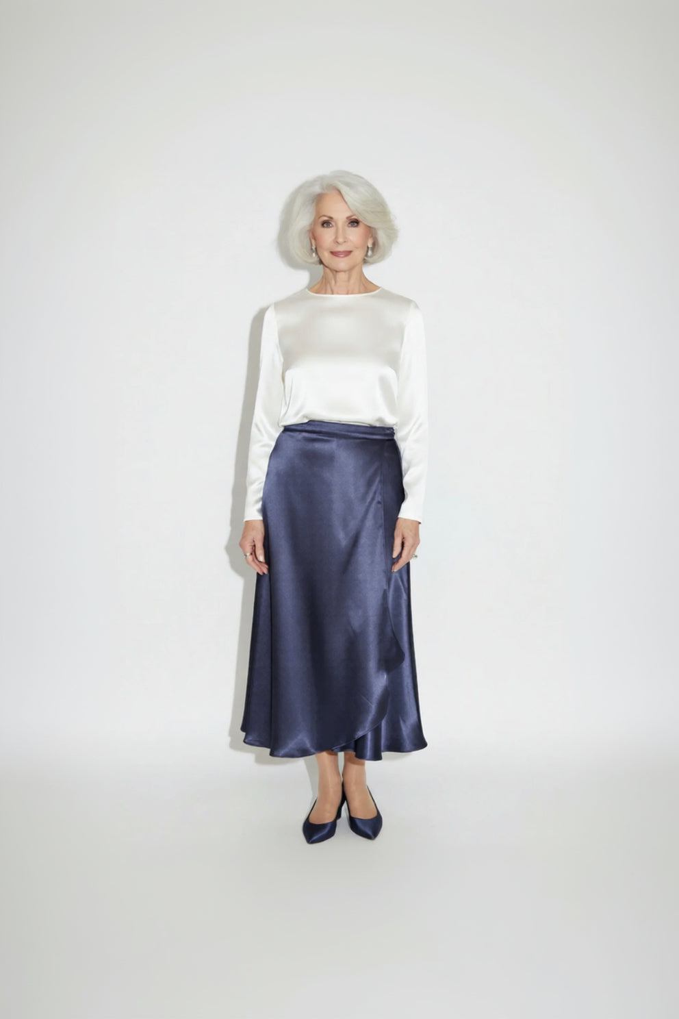 Woman wearing a white blouse and navy satin skirt on a white background