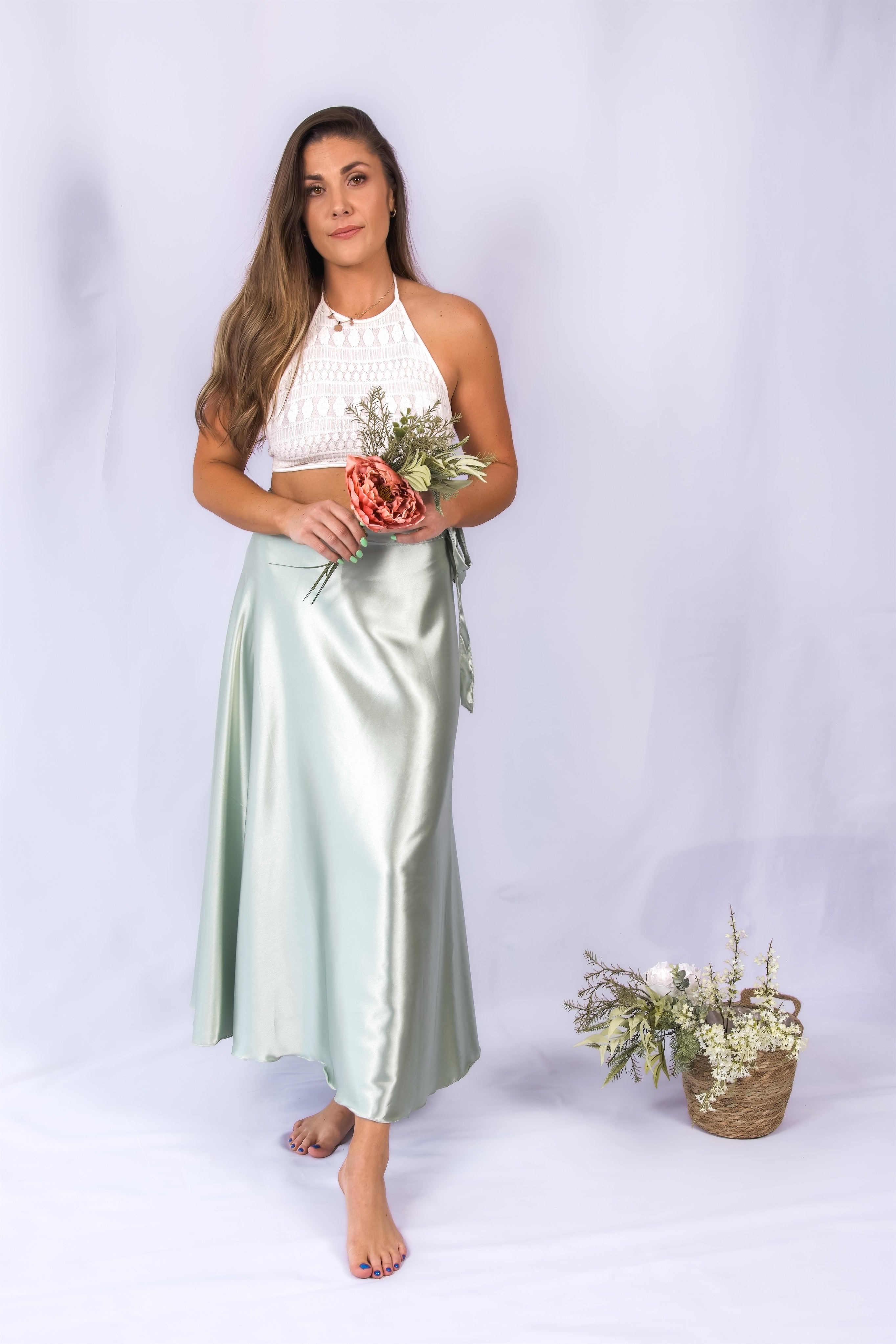 Woman wearing a white top and light green skirt holding flowers on a white background