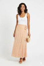 Woman wearing a white tank top and peach skirt with a white background