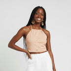 Woman wearing a beige halter top and white pants, holding a woven bag on a white background