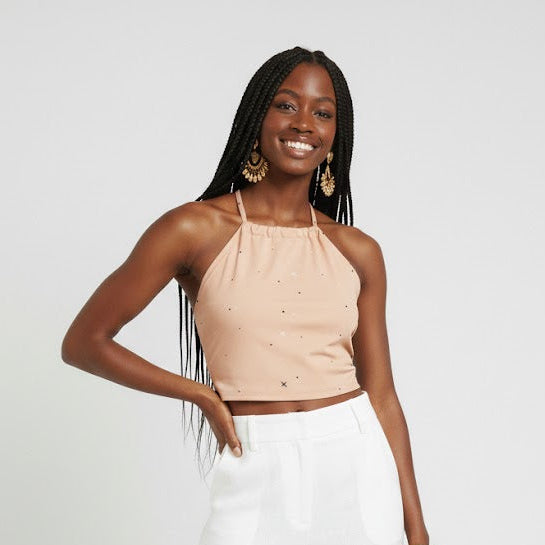 Woman wearing a beige halter top and white pants, holding a woven bag on a white background