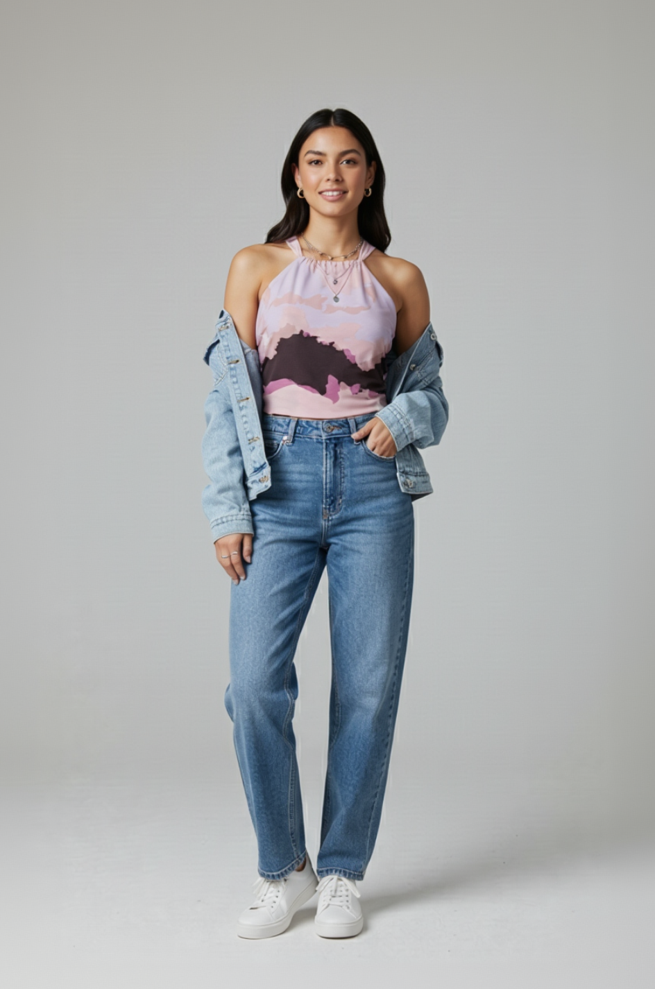 Woman wearing a pink floral top, blue jeans, and a denim jacket on a gray background
