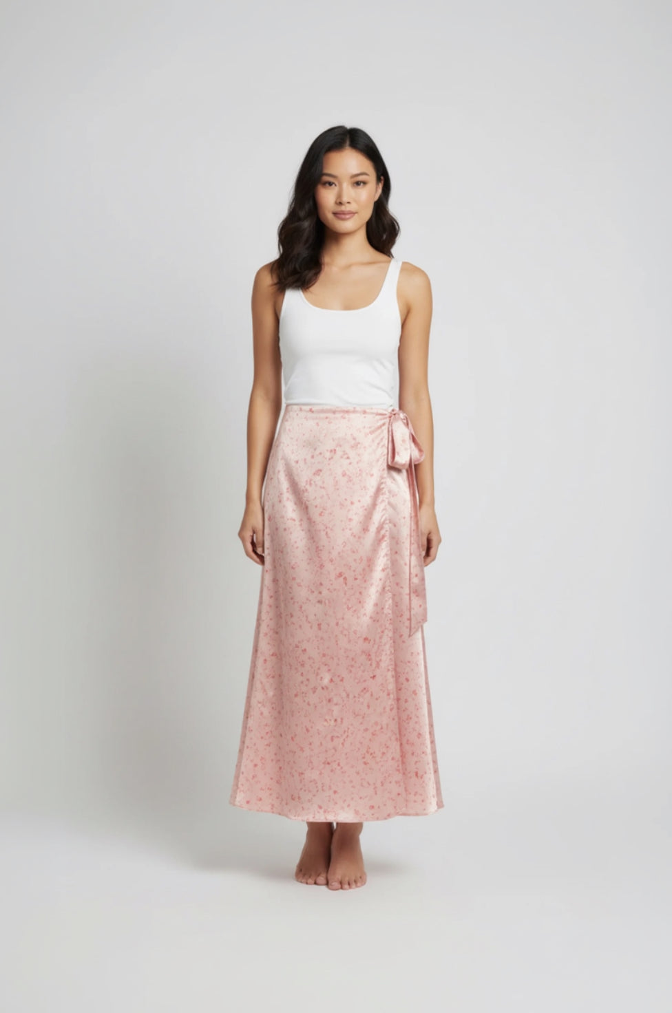 Woman wearing a white tank top and pink floral skirt on a white background