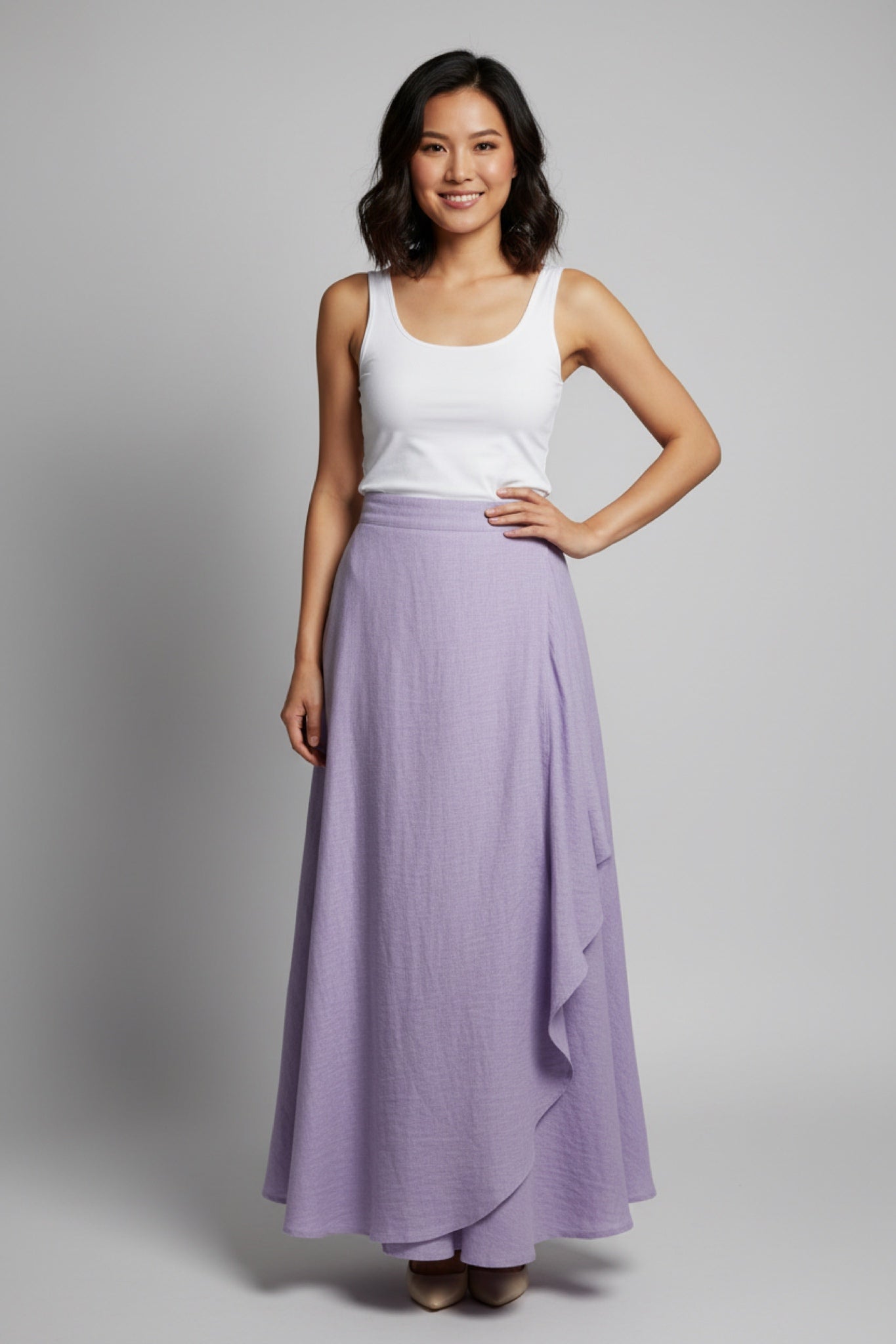 Woman wearing a white tank top and purple linen skirt on a gray background