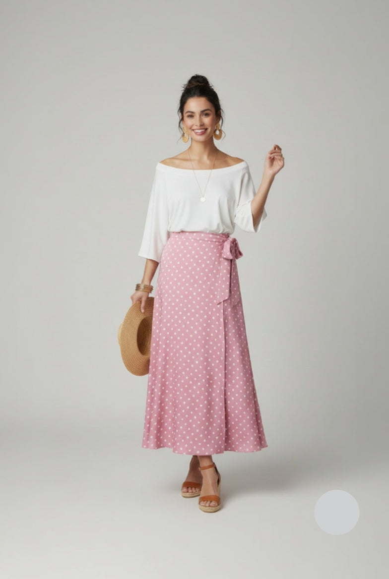 Woman wearing a white blouse and pink polka dot skirt with a straw bag on a light gray background